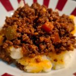 Hearty beef mince with vegetables served over a bed of creamy mashed potatoes on a striped plate
